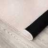 A close-up view of a rug with a beige top and a black underside, resting on a wooden floor. Produktbild-Vorschau