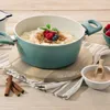 A teal pot filled with rice pudding, garnished with berries and cinnamon, sits on a wooden table with cinnamon sticks and a small bowl of cinnamon sugar. Anteprima dell’immagine prodotto