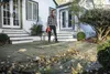 A man is using a leaf blower on a patio in front of a house. Produktbild-Vorschau