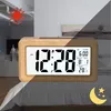 A digital alarm clock is shown on a bed, with a split background indicating day and night. Produktbild-Vorschau