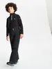 A young boy wearing ski pants and a black top with suspenders, standing against a white background. Produktbild-Vorschau