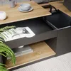 A close-up view of a modern coffee table with a lift-top mechanism, showing its storage compartments and decorative items. Voir les images du produit