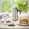 A coffee set with a moka pot, a cup of coffee, sugar cubes, and a pastry on a wooden table. Anteprima dell’immagine prodotto