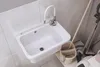 A white sink with a faucet running water, surrounded by cleaning supplies. Anteprima dell’immagine prodotto