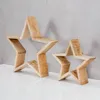 Two wooden star decorations of different sizes are placed on a white surface against a gray concrete wall. Produktbild-Vorschau