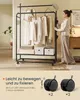 A woman is interacting with a black metal garment rack with clothes on it. The bottom part of the image shows close-ups of the wheels and text in German. Produktbild-Vorschau