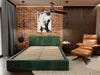 A bedroom scene featuring a green upholstered bed frame, a brown leather armchair with an ottoman, and a brick wall backdrop. Produktbild-Vorschau