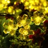 Close-up of yellow LED flower lights with green leaves and some red accents in the background. Produktbild-Vorschau