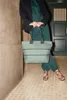 A person holding a sage green tote bag in a hallway. Náhľad obrázku produktu
