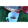 Juice being poured from a fruit press into a white pitcher, set against a grassy background. Produktbild-Vorschau