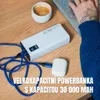 A power bank, charging cable, and earbuds are on a wooden desk next to a cup of coffee and a laptop being used by a person. Voir les images du produit