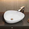 A white oval vessel sink with a chrome faucet and a gold drain sits on a dark gray countertop against a textured tan wall. Anteprima dell’immagine prodotto