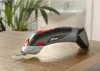 A cordless electric scissors sits on a wooden surface with a plant in the background. Produktbild-Vorschau