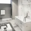A modern bathroom with a marble-tiled bathtub and a concrete shower area. Produktbild-Vorschau