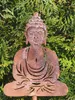 A rusty metal Buddha garden ornament is placed in front of green foliage. Náhled obrázku produktu