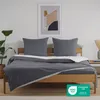 A bed with grey bedding and two pillows, set against a white wall with a framed abstract artwork. Voir les images du produit
