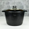 A black speckled pot with a glass lid is placed on a white surface in front of a gray brick wall. Voir les images du produit