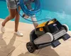 A person is pulling a pool cleaning robot out of a pool. Produktbild-Vorschau