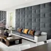 A modern living room with a large upholstered wall paneling, a sofa with decorative pillows, and a coffee table with a piano in the background. Anteprima dell’immagine prodotto