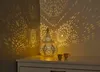 A decorative lantern casting intricate shadows on a wall, placed on a white dresser with two small cups. Produktbild-Vorschau