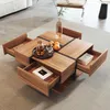 A wooden coffee table with multiple drawers pulled out, displaying books, fruit, and drinks. Produktbild-Vorschau