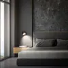 A modern bedroom with a bed, bedside table, and a wall lamp. Anteprima dell’immagine prodotto