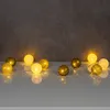 A string of decorative LED lights with spherical bulbs, some with a glittery gold finish and others with a soft yellow glow, arranged on a white surface against a textured gray background. Produktbild-Vorschau