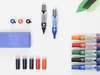 A collection of whiteboard markers, an eraser, and ink refills arranged on a white surface with some green paper leaves. Anteprima dell’immagine prodotto