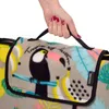A hand holding a folded picnic blanket with a tropical pattern. Produktbild-Vorschau