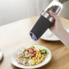 A hand holding an electric pepper grinder over a plate of food. Podgląd zdjęcia produktu