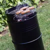 Sausages are being grilled on a black barrel-shaped barbecue in a garden setting. Produktbild-Vorschau