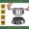 A person's hands are holding a stainless steel fondue pot above an electric fondue base. Produktbild-Vorschau