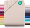 A stack of folded beige fitted sheets with a corner showing the elasticized edge. A row of other colored sheets is visible on the left, and a stack of different colored sheets is visible on the right. Produktbild-Vorschau