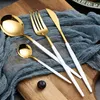 A set of gold and white cutlery laid out on a blue cloth on a wooden board. Voir les images du produit