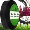 A roll of black garden edging is shown with a label indicating its dimensions and brand. In the background, white stones and pink flowers are visible, with some of the edging installed in grass. Podgląd zdjęcia produktu