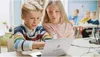 Two children are looking at a laptop in a classroom setting. Produktbild-Vorschau
