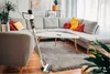 A cordless vacuum cleaner stands upright in a modern living room next to a sofa and coffee table. Produktbild-Vorschau