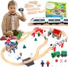 A young boy is playing with a wooden train set, which includes tracks, a train, a police station, a bridge, and various accessories. The set is laid out on a white background, with some packaging visible in the upper right corner. Náhled obrázku produktu