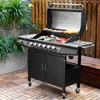 A black gas grill with food cooking on it, placed on a wooden deck with plants in the background. Produktbild-Vorschau