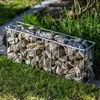 A gabion basket filled with stones, placed on a lawn next to some greenery. Voir les images du produit