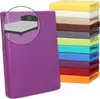 A stack of colorful fitted sheets and a single purple fitted sheet in the foreground with a circular inset showing a bed with a headboard. Produktbild-Vorschau