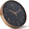 A close-up, angled view of a modern wall clock with a black face and gold numerals and hands, set against a white background. Produktbild-Vorschau