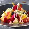 A close-up of a fruit salad with skewers and drizzled with sauce. Produktbild-Vorschau