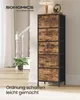 A tall, narrow chest of drawers with a rustic wood-grain finish and black metal frame, placed in a well-lit hallway with a staircase and a potted plant. Produktbild-Vorschau