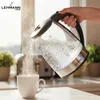 A hand is pouring boiling water from a glass electric kettle into a white mug. Steam is rising from the mug and the kettle. Produktbild-Vorschau