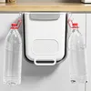 A white and gray hanging trash can with red hooks is shown, with two large plastic water bottles hanging from the hooks. Produktbild-Vorschau