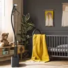 A nursery room with a teddy bear, a garment steamer, a crib with a yellow blanket, and wall decor. Produktbild-Vorschau