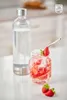 A clear glass bottle of sparkling water and a glass jar filled with sliced strawberries and ice, garnished with a strawberry and mint leaf, sit on a countertop. Produktbild-Vorschau