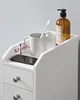 A close-up view of a white bathroom storage unit with drawers, a shelf, and items like a toothbrush, mug, phone, and soap dispenser. Náhled obrázku produktu
