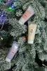 Three small tubes of hand cream are placed on the branches of a frosted Christmas tree, adorned with colorful lights. Produktbild-Vorschau